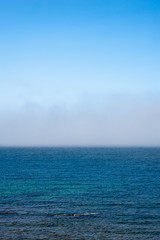 Fog low over wavy water under blue sky