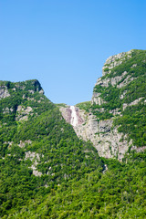 Fototapeta na wymiar Steep cliffs covered in trees with distant waterfall under blue