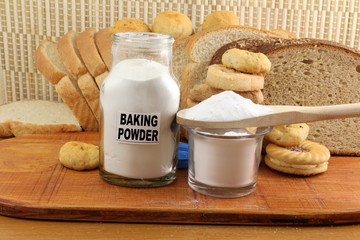 baking powder in a glass jar and wooden spoon with cookie and bread