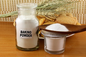 baking powder in a glass jar and wooden spoon with cookie and bread