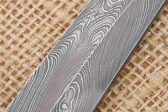 Fragment of the traditional handmade Finnish knife blade with the abstract wave pattern of damascus steel over an old sack background.