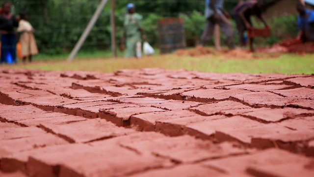 Extreme close up of red bricks drying in the sun; a boy adds more to the rows