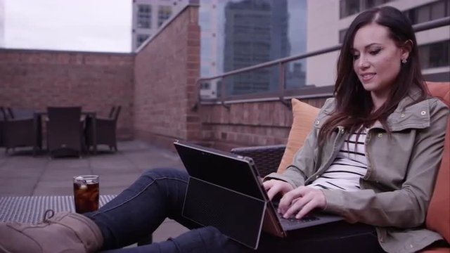 Panning view of woman relaxing on roof top using laptop.