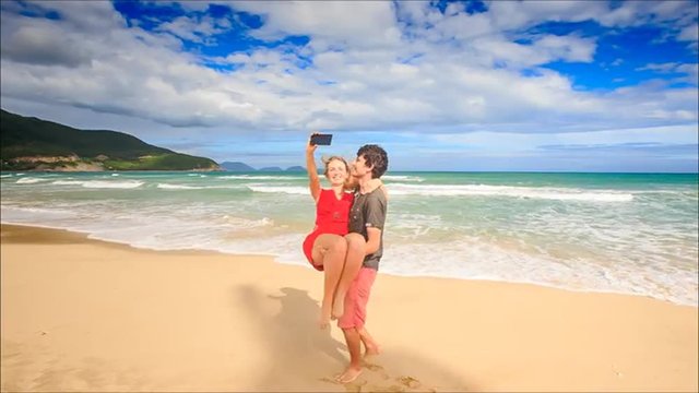 Guy Holds in Arms Circles Blond Girl Makes Selfie on Beach