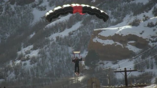 Slow motion footage of a parachute-wearing skiier landing on a snowy mountain slope