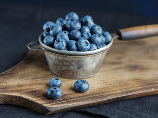 Blueberries in a metal bowl on a wooden board on a dark background