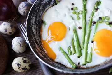 Country breakfast, fried eggs, bread, asparagus and onions on a wooden background, close-up