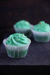 Cupcakes with green cream on a wooden textured board on dark background