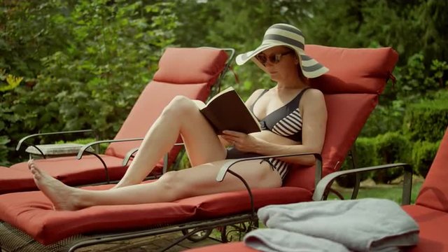 An older woman reading by the pool sees something and gets up, in slow motion