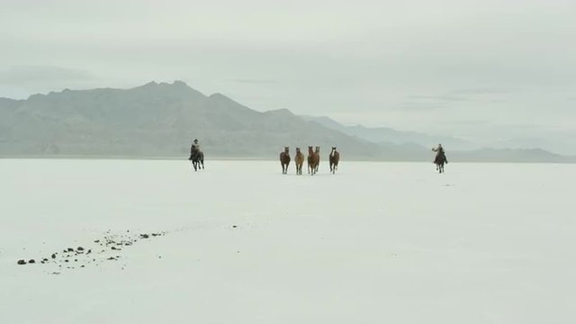 Horses running with cowboys riding across salt flats.
