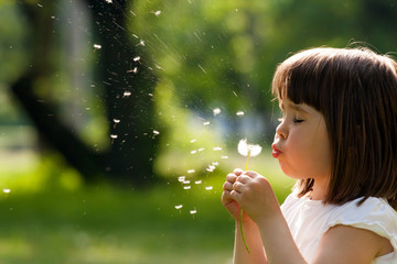 Beautiful child with dandelion flower in spring park. Happy kid having fun outdoors.