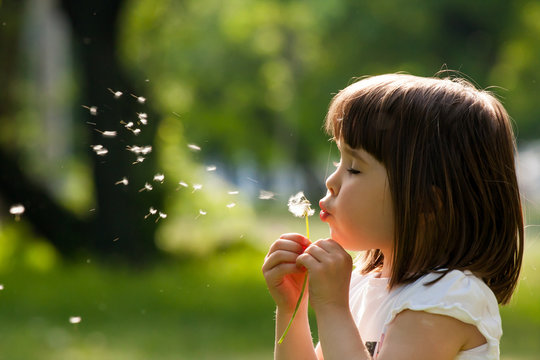 Beautiful child with dandelion flower in spring park. Happy kid having fun outdoors.