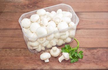 Button mushrooms in a plastic tray on a wooden surface