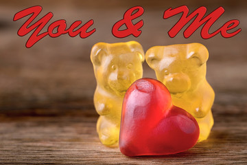 macro two yellow gummy bears with red hearts and you & me written on wood