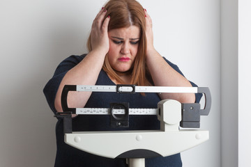 worried woman on a medical weight scale - obrazy, fototapety, plakaty
