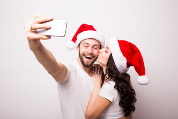 christmas, holidays, technology and people concept - happy couple in santa hats taking selfie...