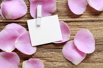 Blank paper card and pink rose petals on wooden background