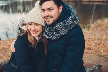 happy couple in warm knitted hat and scarf walking outdoor in autumn forest, cozy mood