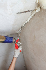 Worker's hand fix a rent in wall using polyurethane foam