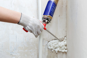 Worker's hand fix a rent in wall using polyurethane foam - obrazy, fototapety, plakaty
