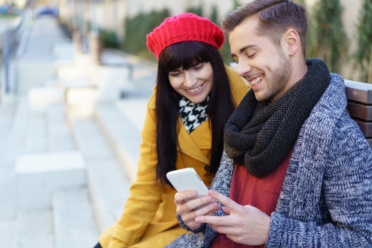paar sitzt in der stadt und schaut l&auml;chelnd auf ein smartphone