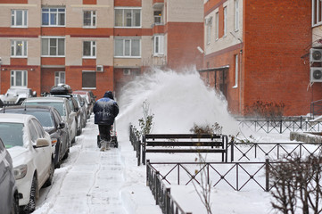 man removes snow in the yard of a multistory building with snow