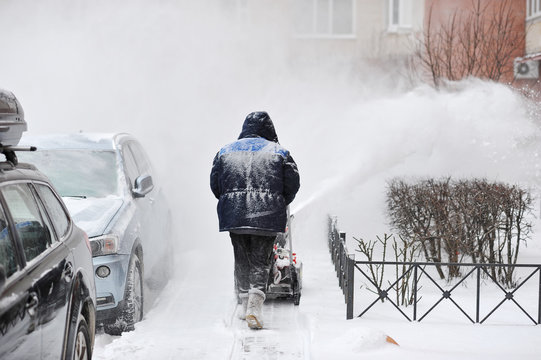 man removes snow in the yard of a multistory building with snow