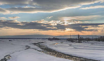 Georgia, Kakheti, Alazani Valley. Riverbanks river Kabali, covered with snow on the background of sunset.
