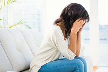 Woman holding her head while sitting on the couch