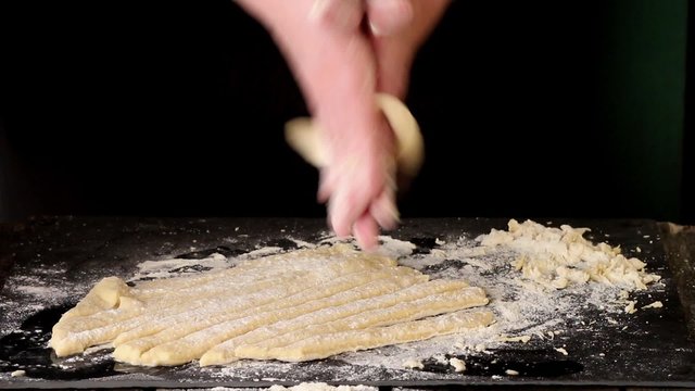 Female hands making pasta pici over black kitchen table, powdering by flour