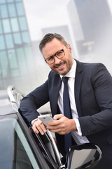 Taxi driver standing by car outside and using smartphone