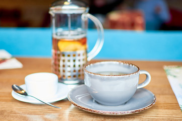 Cup of tea and teapot on wooden table in cafe