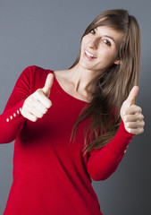 optimism concept - shy beautiful young woman smiling with thumbs up in the foreground for fun happiness, studio grey background