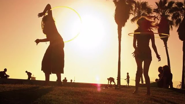 Slow motion shot of two women playing hula hoops with lens flare near Venice Beach, California