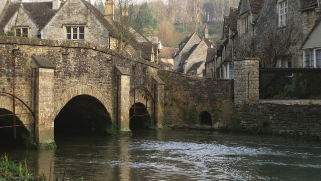 Tilt from a stone bridge over a stream to a stone village in England.