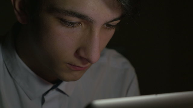 Close-up of young handsome man using tablet pc in the dark