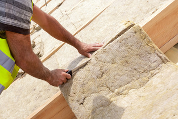 Roofer builder worker installing roof insulation material on new house under construction. Cutting...
