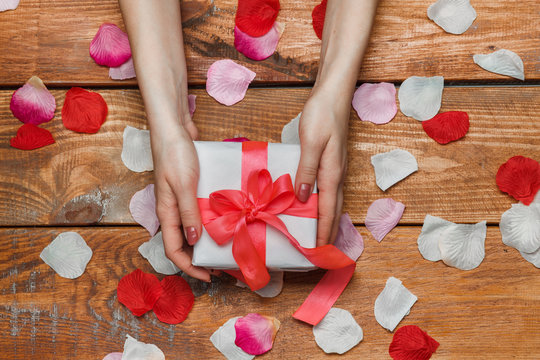 Valentines Day gift and Female hands on wooden background with petals