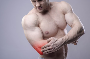 Athletic muscular man has pain in the elbow. Red spot of injury