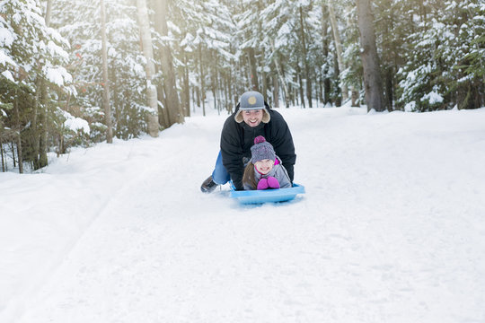 Young happy father and her daughter enjoying a sledge ride 