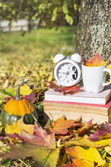 books with coffee cup and clock on a colorful leaves background - autumn concept