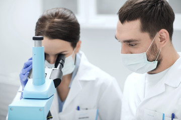 scientists in masks looking to microscope at lab