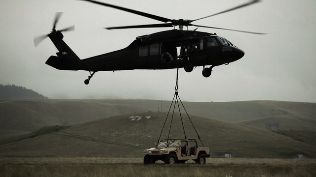 Shot of Black Hawk helicopter hauling off Humvee from field.
