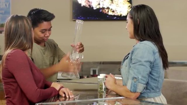 Customers at a recreational marijuana shop being shown a large bong from behind the counter