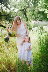 Mom and daughter in nature with a bouquet of wild flowers, family, family values, childhood, lifestyle