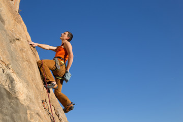 Young male climber hanging by a cliff.