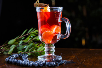 Red fruit tea with tangerines and cinnamon in a glass mug.