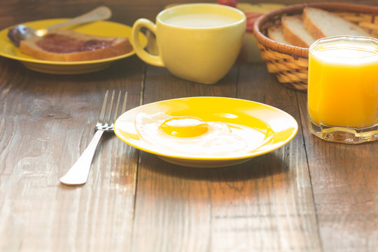 Breakfast served in yellow tableware - eggs, oatmeal, orange juice, milk, on wooden background