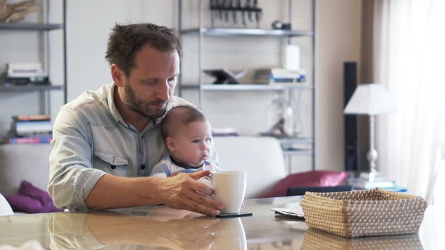 Sleepy, tired father with his baby boy drinking coffee at home