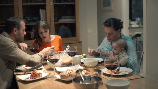 Young group of friends talking, using smartphone and eating dinner at home
